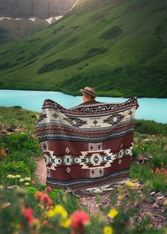 a person sitting on the ground with a blanket over their head and mountains in the background