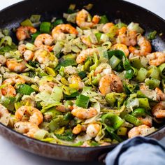 a skillet filled with shrimp and vegetables on top of a white countertop next to a blue towel