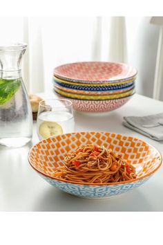 a bowl filled with pasta sitting on top of a table next to plates and glasses