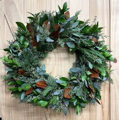 a wreath with green and brown leaves hanging on a wooden wall