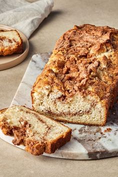 a loaf of cinnamon swirl bread sitting on top of a marble platter next to two slices