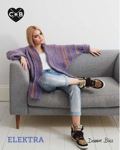 a woman sitting on top of a couch next to a gray sofa covered in a knitted blanket