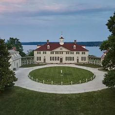 an aerial view of a large house with a circular lawn in the foreground and trees surrounding it