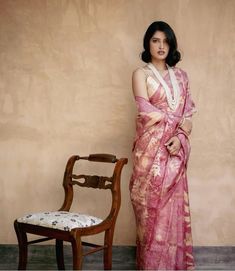 a woman in a pink sari standing next to a chair and looking at the camera