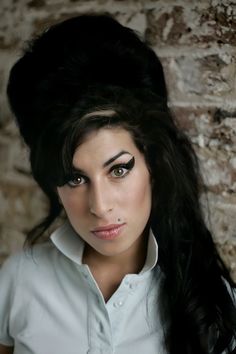 a woman with long black hair wearing a white shirt and posing in front of a brick wall