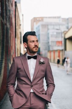 a man in a suit and bow tie is standing on the street with his hands in his pockets