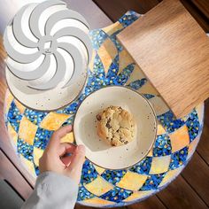 a person holding a plate with a muffin in it on top of a table