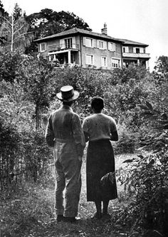 an old photo of two people walking in front of a house