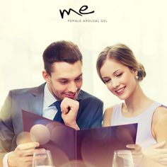 a man and woman sitting at a table looking at an open book with wine glasses on it