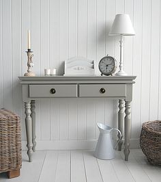 a table with a clock, lamp and vase on it in a room that has white walls