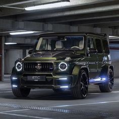 a green jeep is parked in an underground parking garage with its lights on and it's hood up