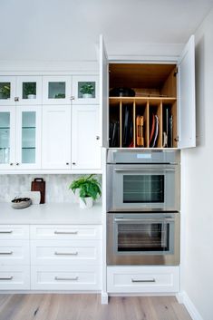 a kitchen with white cabinets and stainless steel ovens in the center, open cupboards on both sides