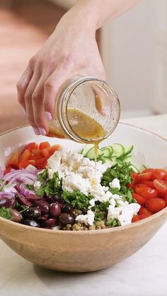 a person pouring dressing over a salad in a bowl