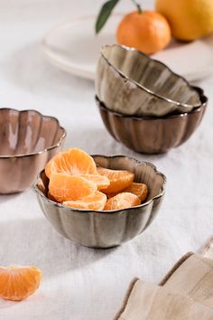 three metal bowls filled with oranges on top of a white table cloth next to plates and utensils