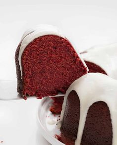 a piece of red velvet cake with white icing being lifted from the bundt cake