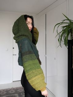 a woman wearing a green and black knitted hoodie over her head, standing in front of a door