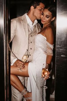 a man and woman standing next to each other in front of a metal door holding wine glasses