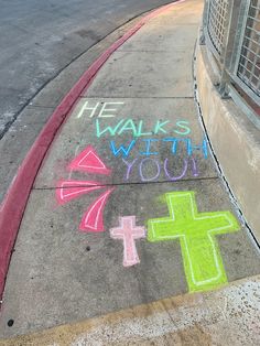 the sidewalk has chalk drawings on it with words written in different colors and shapes, along with a cross