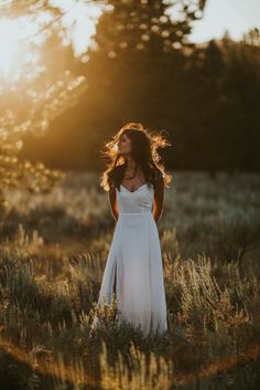 a woman in a white dress is standing in the grass with her hair blowing in the wind