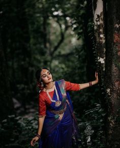 a woman standing next to a tree in the woods