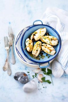 a blue and white bowl filled with food next to silverware on top of a table