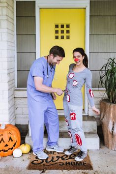 a man and woman in scrubs stand on the front steps of a house decorated for halloween