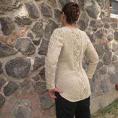 a woman standing in front of a stone wall with her back turned to the camera