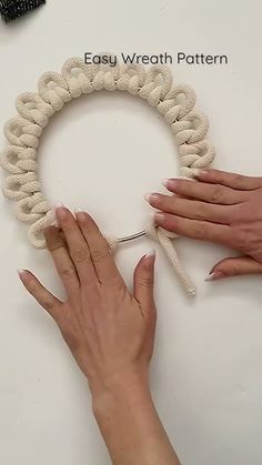 two hands are working on a wreath with yarn