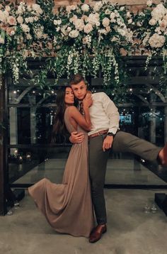 a man and woman are posing in front of a flower covered arch with flowers on it