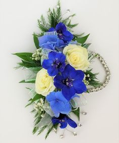 blue and yellow flowers are arranged on a white table top with pearls, greenery, and beads