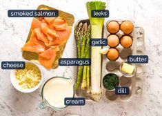 the ingredients for an asparagus salad laid out on a marble counter top, including eggs, broccoli, cheese and other vegetables