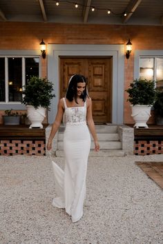 a woman in a white wedding dress is walking towards the front door of a house