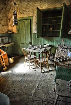 an old fashioned kitchen with green walls and wooden furniture, including two dining tables and four chairs