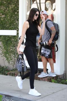 a woman in black top and leggings walking past a man wearing white sneakers