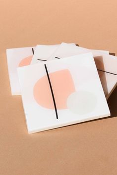 four square coasters with pink and white shapes on them sitting on a brown surface