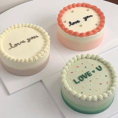 three decorated cakes sitting on top of a white table next to each other, one with the word love u written on it