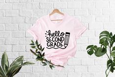 a pink shirt with the words hello second grade printed on it next to a potted plant