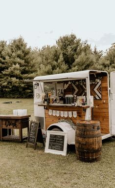 an old fashioned food truck is set up in the grass with two wooden barrels next to it