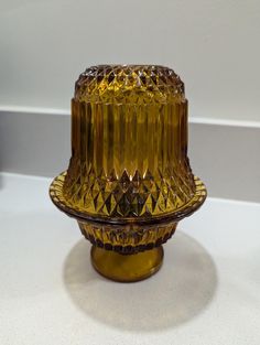 a yellow glass candle holder sitting on top of a table next to a white wall