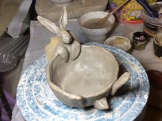 a ceramic bowl with a rabbit in it sitting on a table next to other pottery