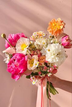 a bouquet of flowers is being held up by someone's hand in front of a wall