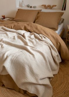 an unmade bed in a bedroom with brown linens and pillows on the floor