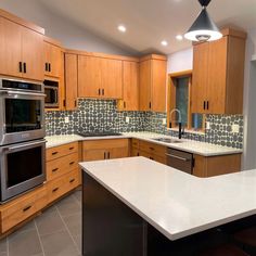 a kitchen with wooden cabinets and white counter tops, stainless steel appliances and an island in the middle