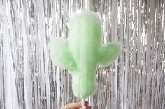 a person holding up a green cotton candy cactus in front of tinsel foil curtain