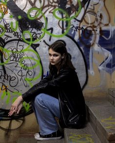 a woman sitting on the ground in front of graffiti