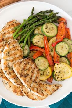 a white plate topped with chicken and veggies on top of a blue table cloth