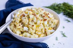 a white bowl filled with potato salad next to two silver spoons on a blue napkin