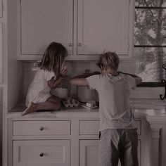 two children are sitting on the kitchen counter and one is reaching for something in the sink