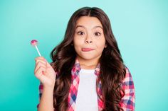 a young woman holding a lollipop in her hand and looking at the camera