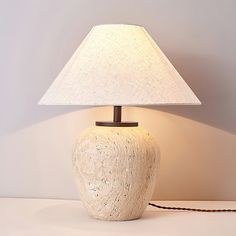 a lamp that is sitting on top of a table next to a white vase with a brown base